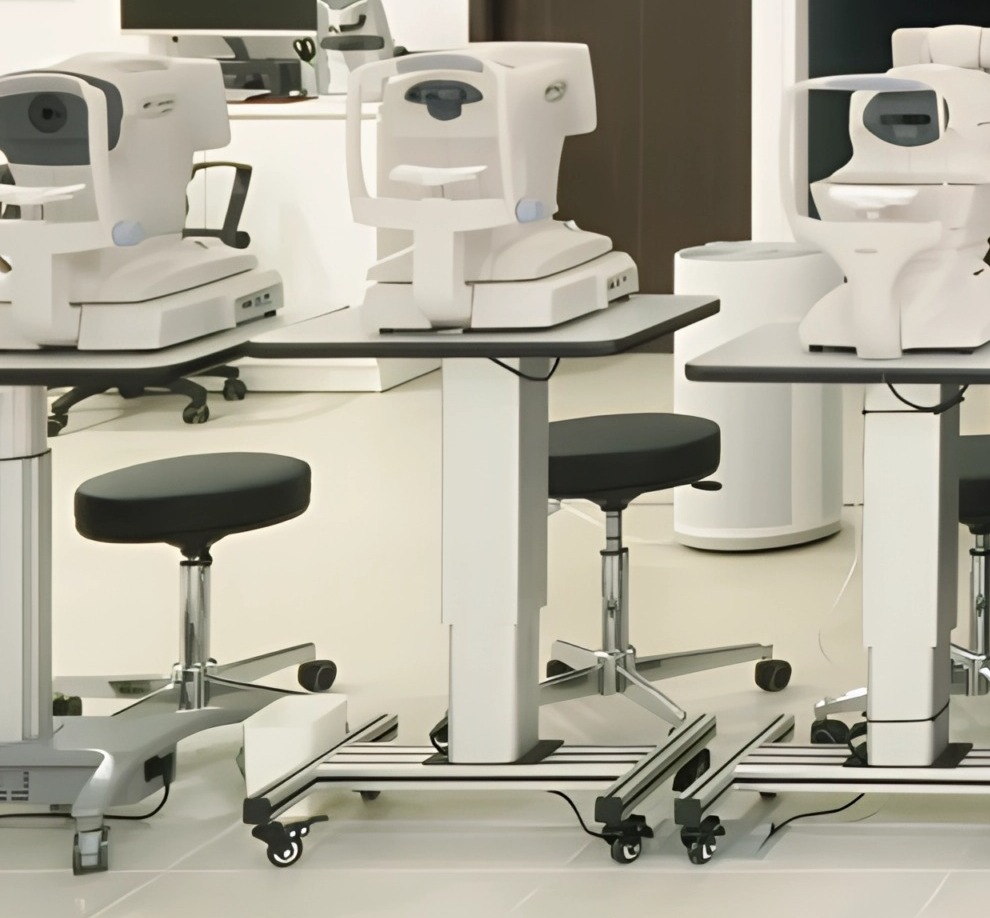 Row of white eye-measurement instruments on height-adjustable tables with black stools in a bright diagnostics room